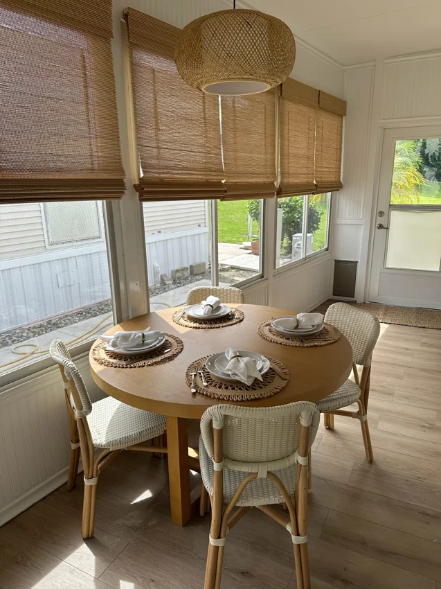 A round dining table with woven pendant lighting beside sunny windows.